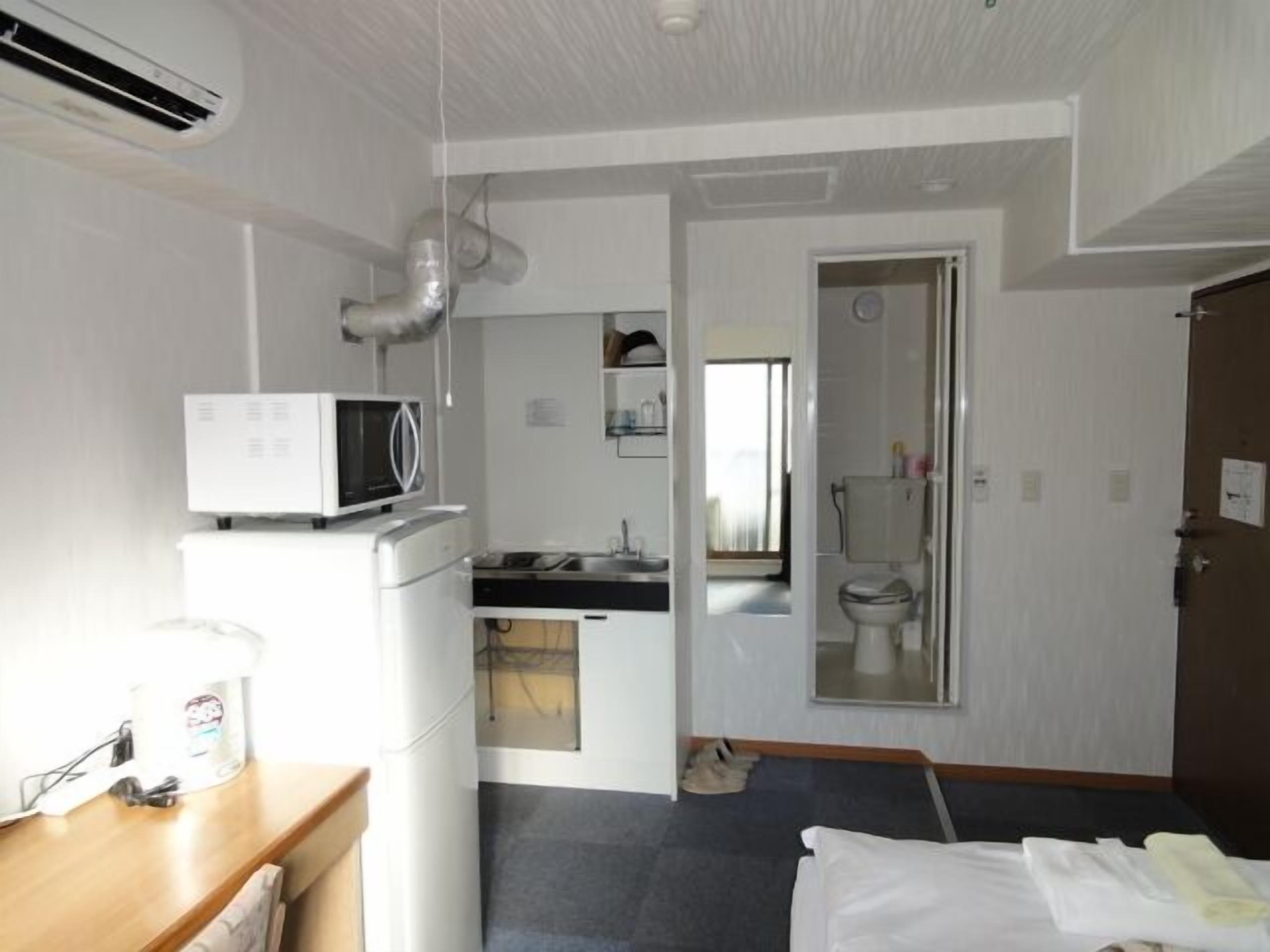 A compact hotel room with a kitchenette, a bed, a bathroom, and a view of the outside.