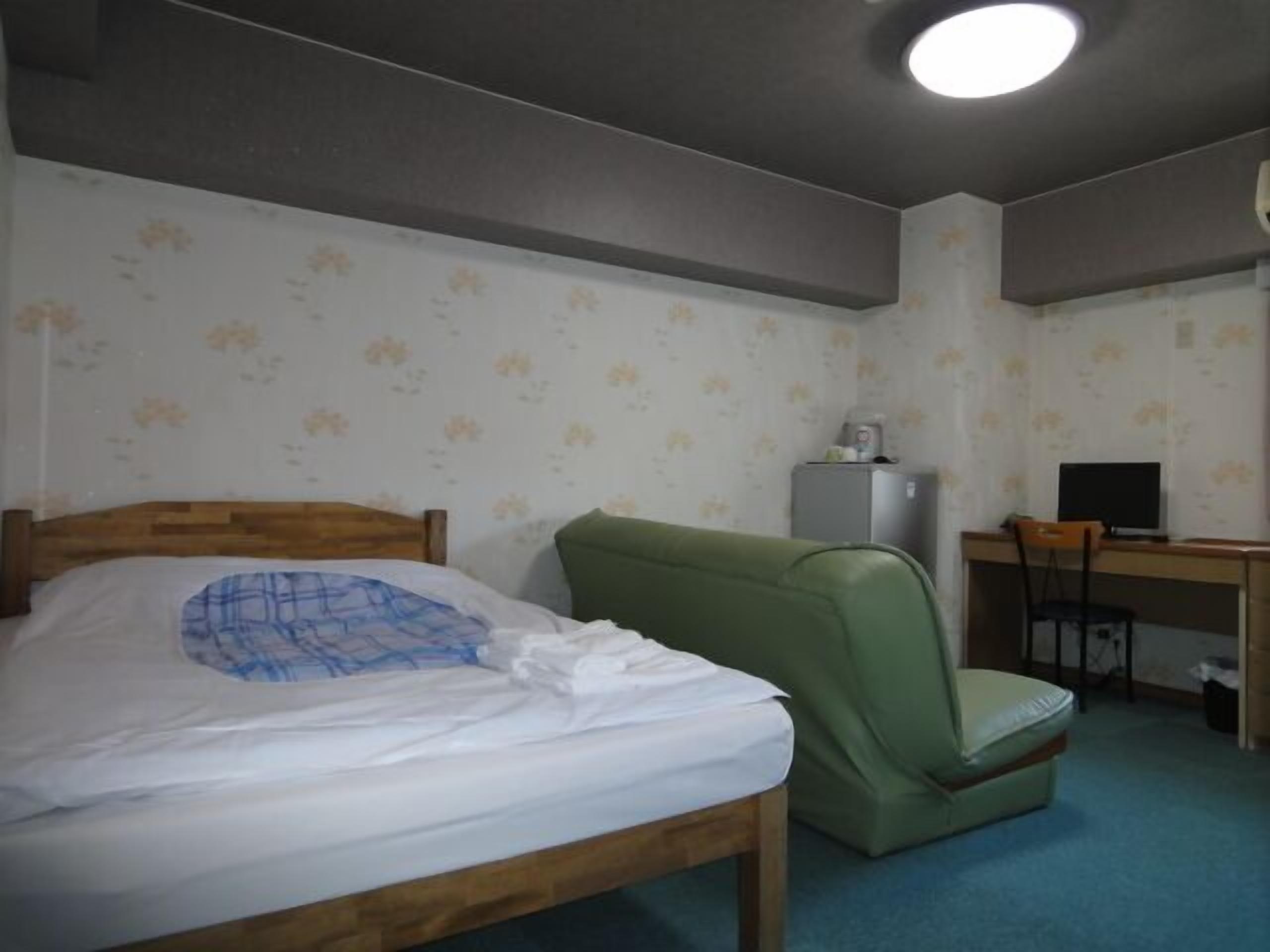 A room with a bed, a desk, a chair, and a refrigerator.