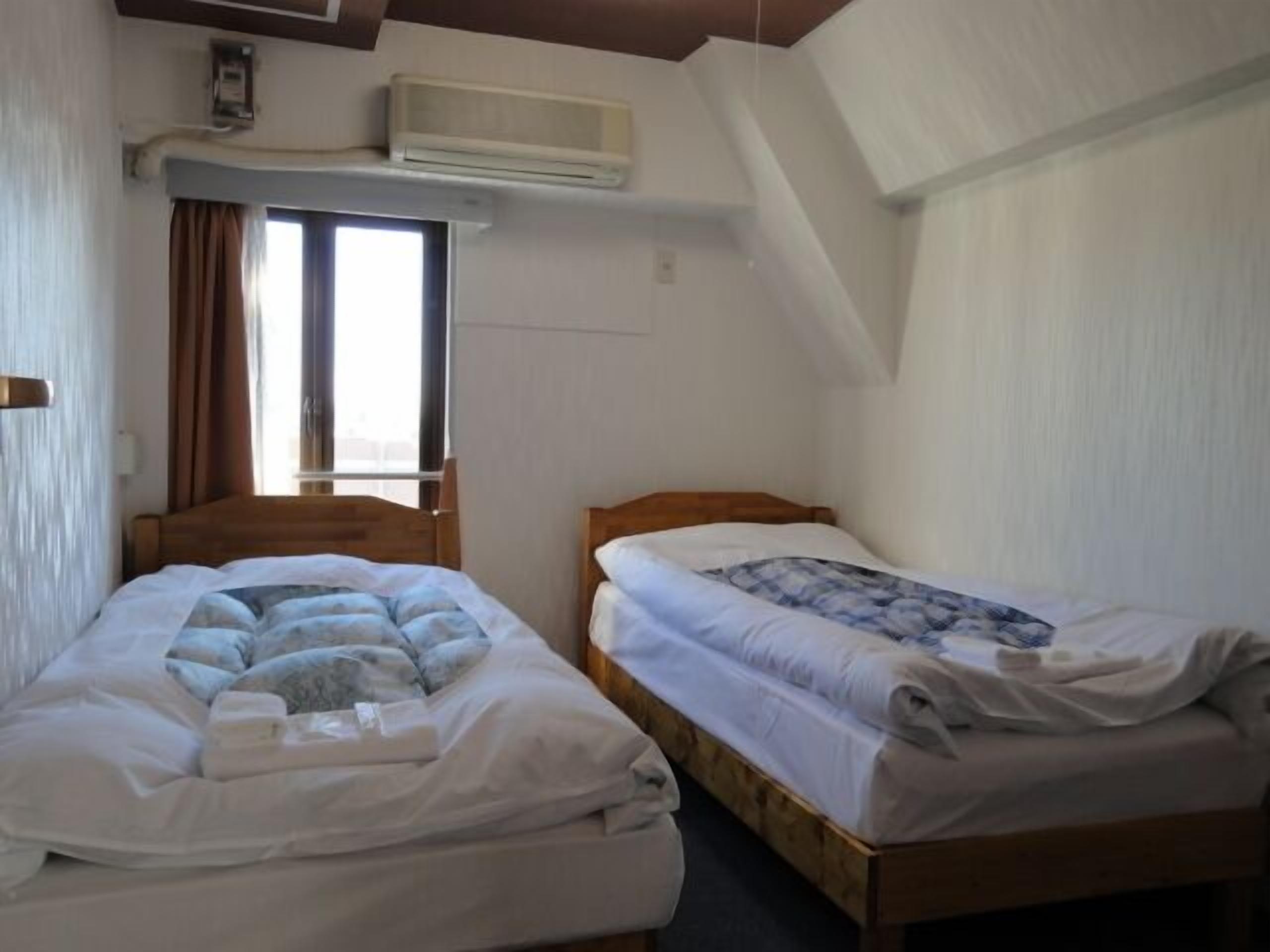 A room with two beds, a window with curtains, an air conditioning unit, and a wooden ceiling.
