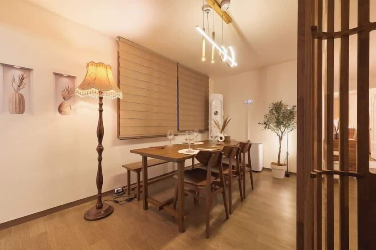 A dining area with a wooden table, chairs, a floor lamp, and a ceiling light fixture.