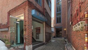 A narrow alleyway with a brick building featuring a glass entrance and a sign with Chinese characters. - Sohwa Mansion [8min STN] / Luggage Keep available (Seoul)