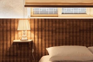 Una habitación con pared de listones de madera, una lámpara de noche, una cama con almohada y una ventana con diseño geométrico.
