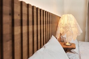 Una cama con ropa de cama blanca, cabecera de madera y una lámpara de mesa con pantalla de encaje.