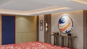 A hotel room with a patterned bedspread, a large abstract painting on the wall, a wooden console table with decorative items, and a door with a red frame. - Zone by The Park New Market Kolkata (Kolkata)
