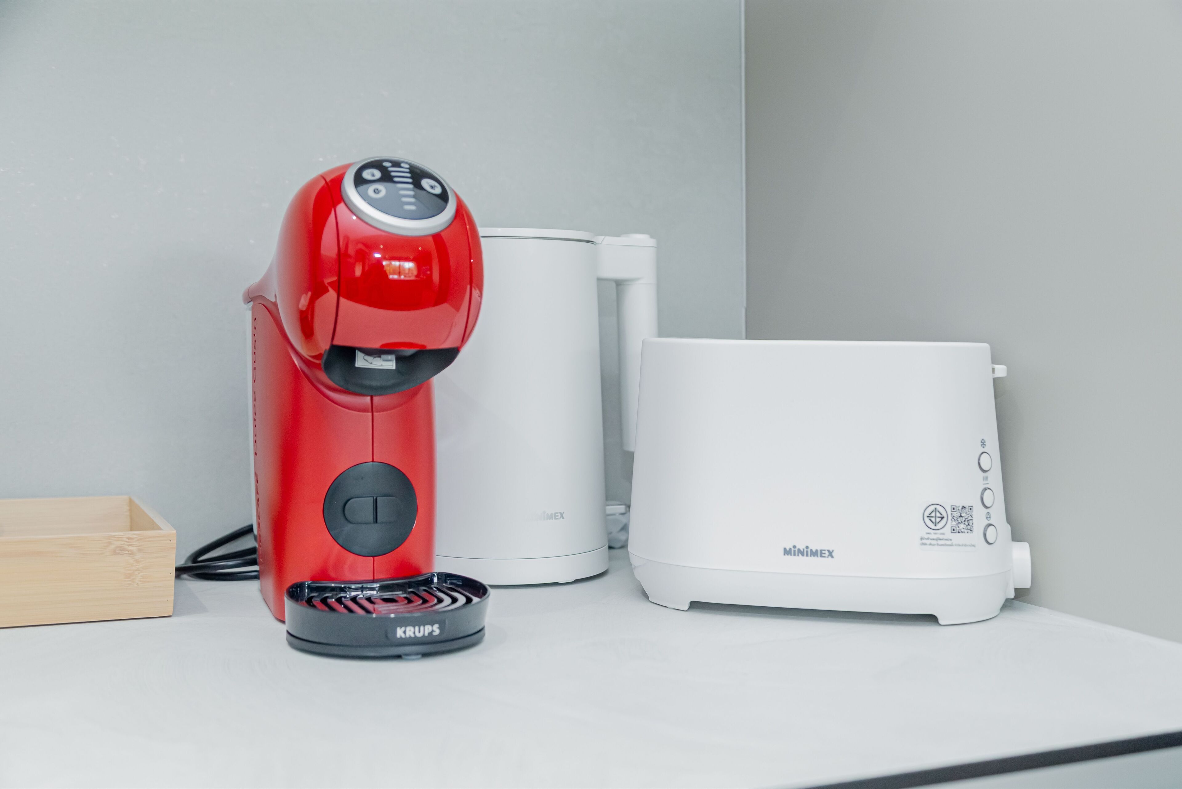 Una cafetera roja, una cafetera blanca y un hervidor eléctrico blanco sobre una encimera blanca.