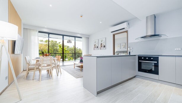 A modern kitchen with a central island, built-in oven, and large windows overlooking a balcony. - Beachside 2BR 200 m to BangTao beach (Choeng Thale)