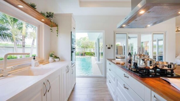 A modern kitchen with white cabinets, a wooden countertop, and a view of a pool. - Kira Japandi Escape with Sauna & Rooftop cinema (Hua Hin)