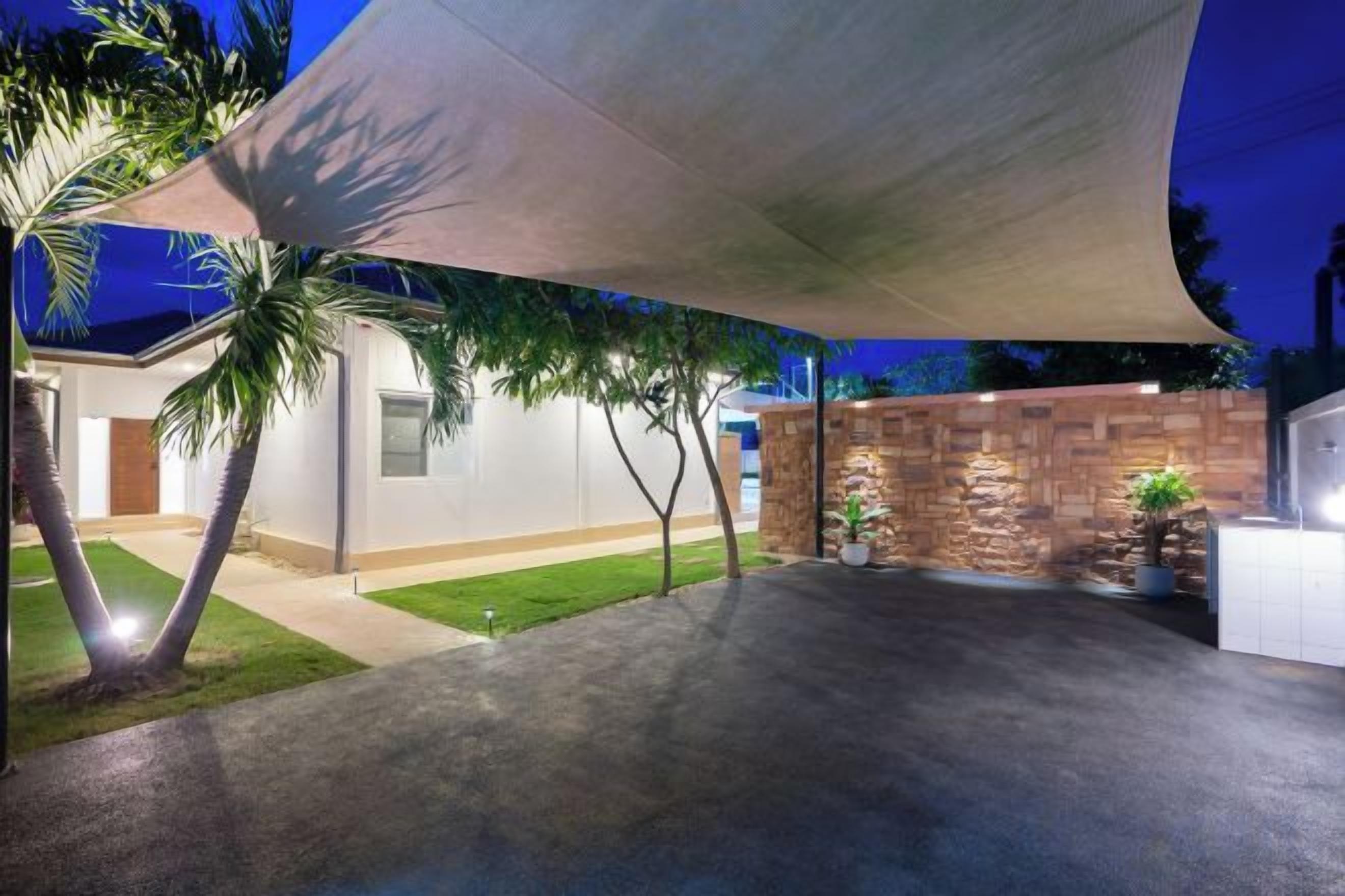 A covered outdoor area with a concrete floor, palm trees, and a stone wall.