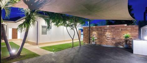 A covered outdoor area with a concrete floor, palm trees, and a stone wall.