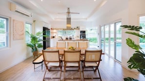 A spacious kitchen with a central island, large windows, and a ceiling fan. - Kira Japandi Escape with Sauna & Rooftop cinema (Hua Hin)