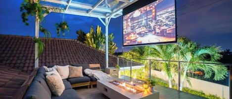 An outdoor seating area with a sofa, a fire pit, and a large screen.