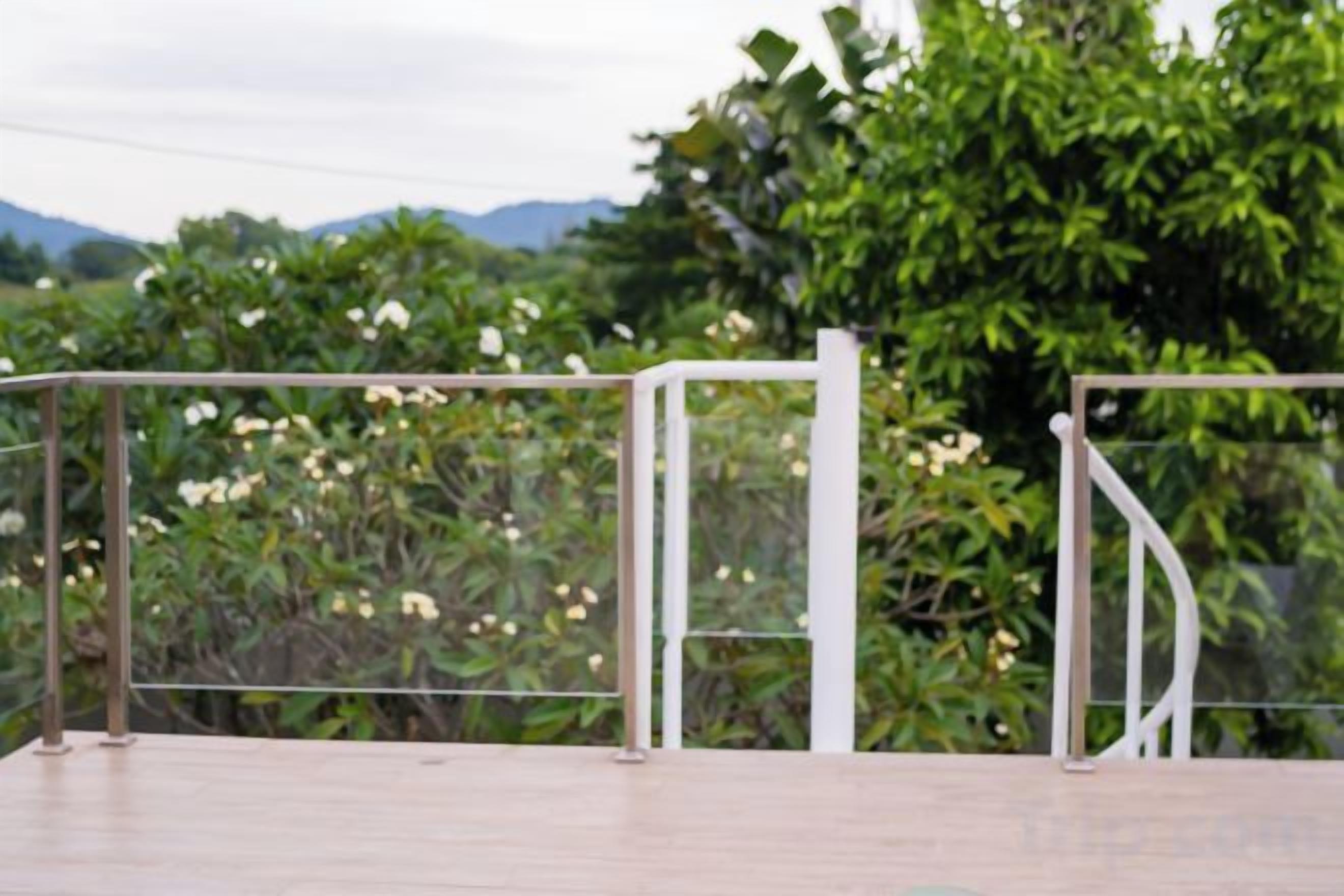 A wooden deck with a metal railing, surrounded by lush greenery and flowering plants.