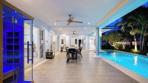 A spacious indoor pool area with a dining table and chairs, ceiling fans, and a view of the pool. - Kira Japandi Escape with Sauna & Rooftop cinema (Hua Hin)