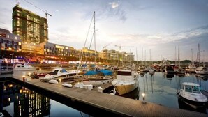 Un port de plaisance avec des bateaux amarrés, une jetée en bois et un bâtiment illuminé en arrière-plan.