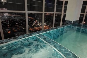 Une chambre d’hôtel située dans un immeuble de grande hauteur, avec une grande fenêtre donnant sur le paysage urbain illuminé la nuit.