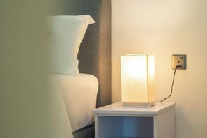 Una cama con ropa de cama blanca y una mesita de noche con lámpara.