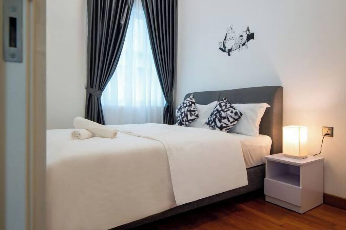 Un lit bien fait, avec une couette blanche et des coussins à motifs, une table de chevet avec une lampe et un élément décoratif mural.