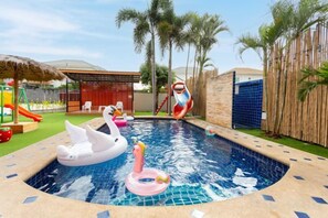 Una piscina con patos y cisnes inflables, un tobogán y un área vallada con palmeras.
