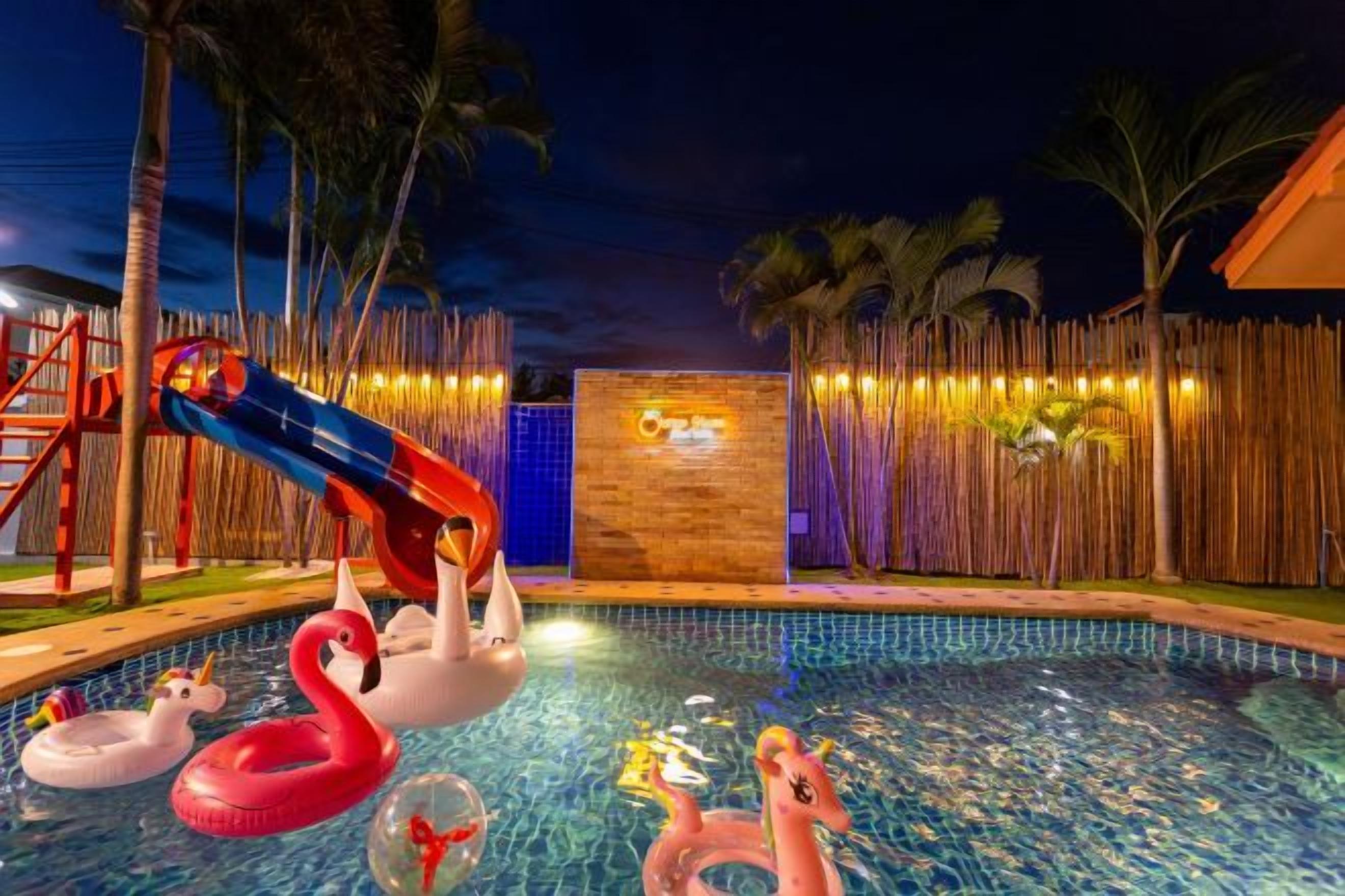 A swimming pool with inflatable swan and flamingo toys, a wooden fence, and palm trees.