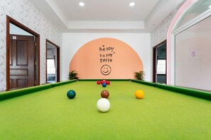 Una mesa de billar con bolas en una habitación con un mural grande que dice 'happy smile' y una puerta a la izquierda.