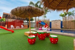 A pool area with artificial grass, a slide, and decorative strawberry-themed planters.