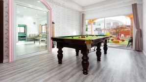 Une table de billard dans une pièce dotée d’une porte vitrée donnant sur un autre espace, d’un plancher en bois et offrant une vue à travers la vitre.