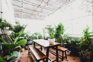 Un área de patio con una mesa y bancos de madera, rodeada de plantas en macetas.