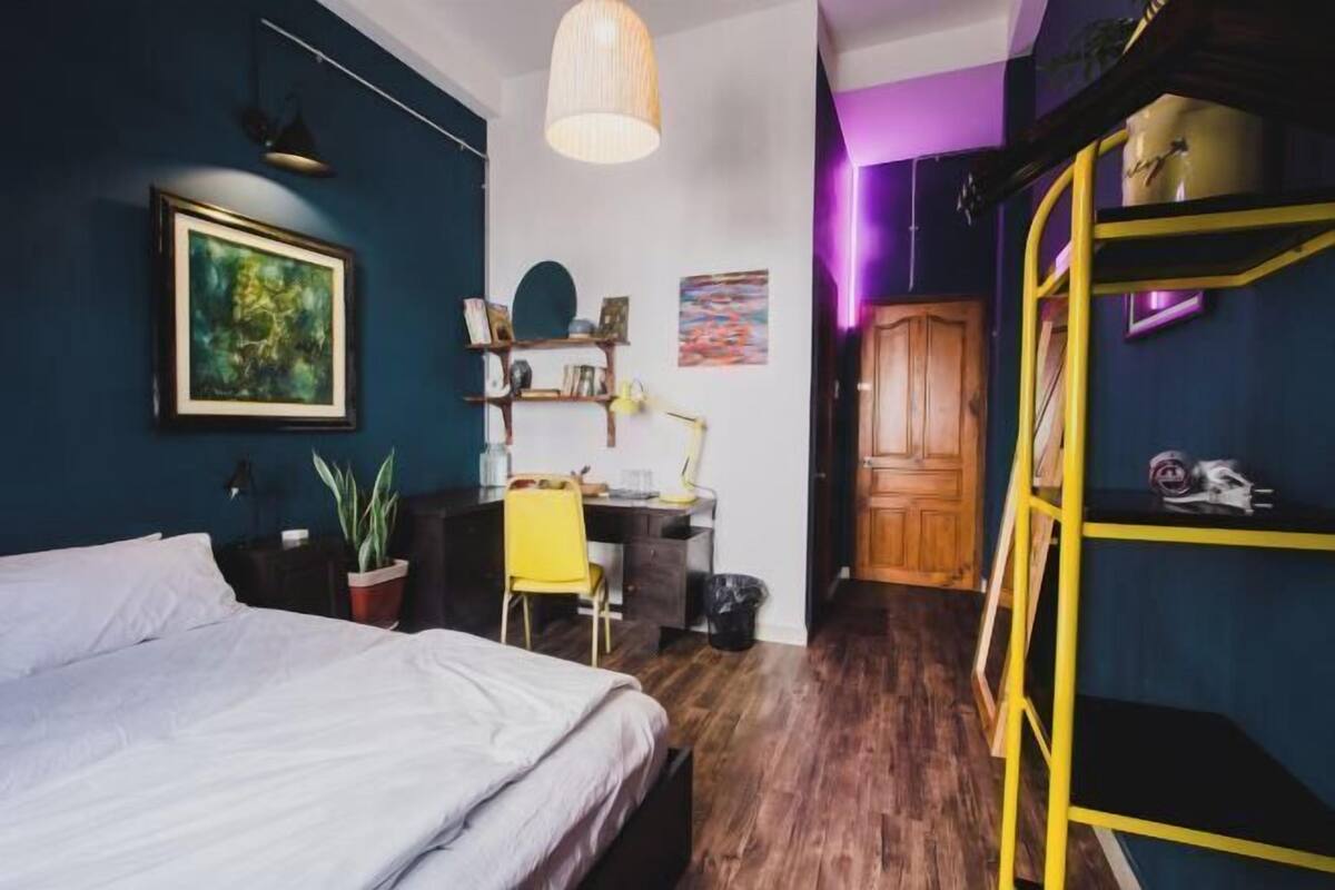 A bedroom with a bed, desk, chair, potted plant, and a bunk bed with a ladder.