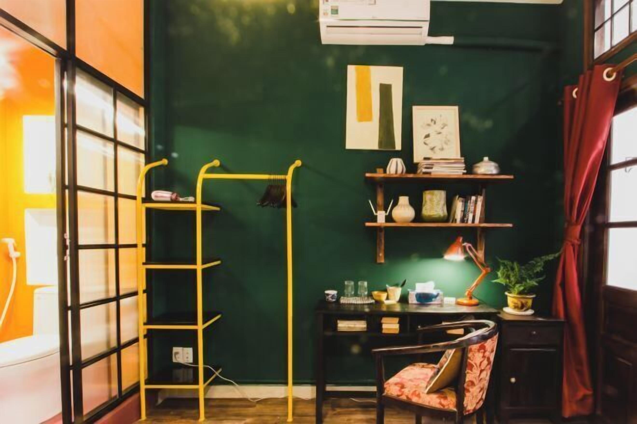 Une pièce avec un mur vert, une échelle jaune, un bureau avec une lampe et une chaise.