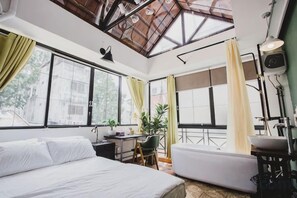 Un dormitorio con cama, escritorio, sillón, sofá y ventanas grandes.