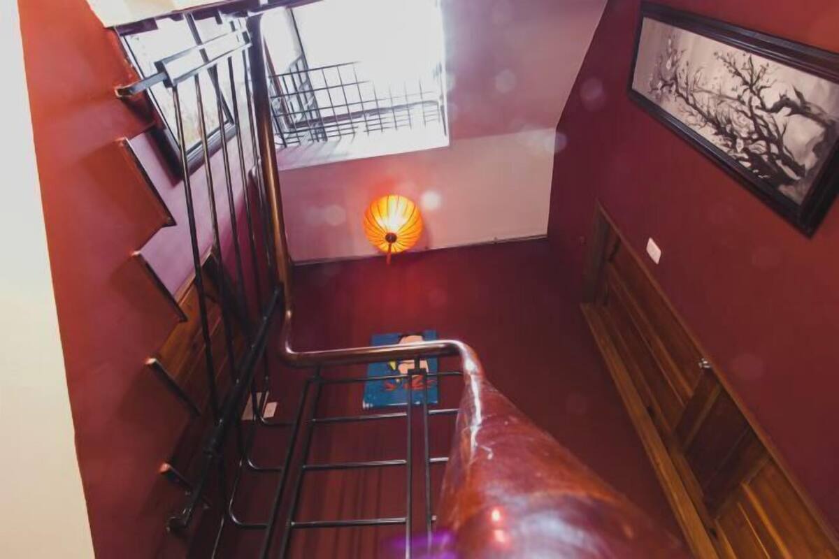 A staircase with a metal railing, a wooden handrail, and a view of a room with a red wall and a framed picture.