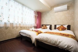Ein Hotelzimmer mit zwei Betten, blumigen Vorhängen, einem gemusterten Wandteppich und einer Klimaanlage.
