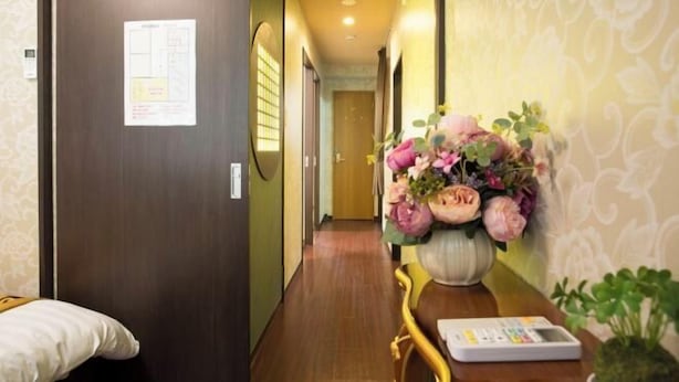A hotel hallway with a wooden floor, a reception desk with a vase of flowers, and a door with a notice.