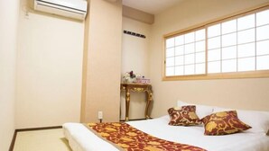 A hotel room with a bed, a window, a small table with decorative items, and an air conditioning unit.