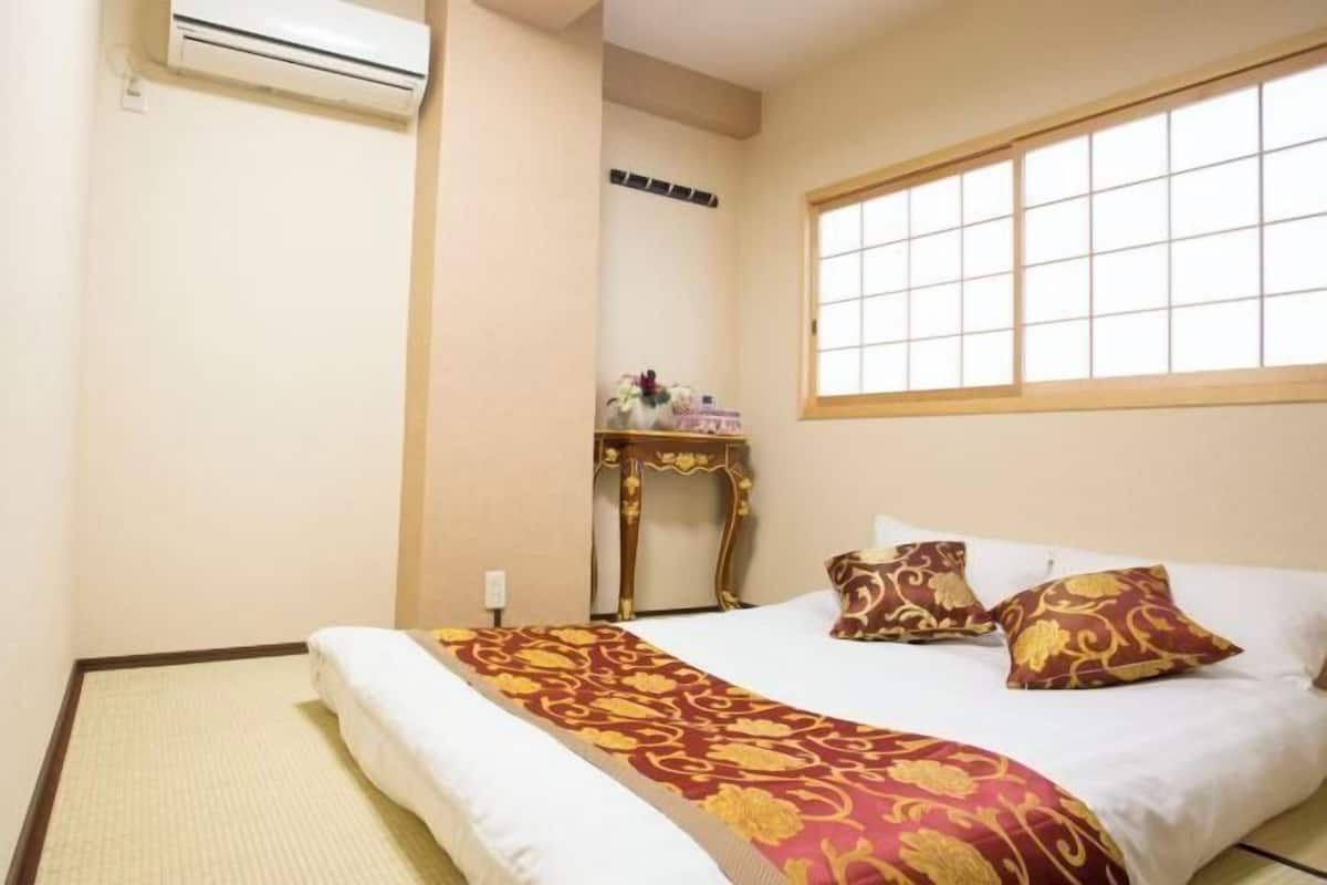 Ein Hotelzimmer mit Bett, Fenster, einem kleinen Tisch und dekorativen Accessoires sowie einer Klimaanlage.