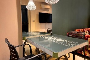 A dining area with a glass table, black chairs, and a television mounted on the wall. - Large Caribbean 1BR Condo near Jomtien Bus Station (Pattaya)