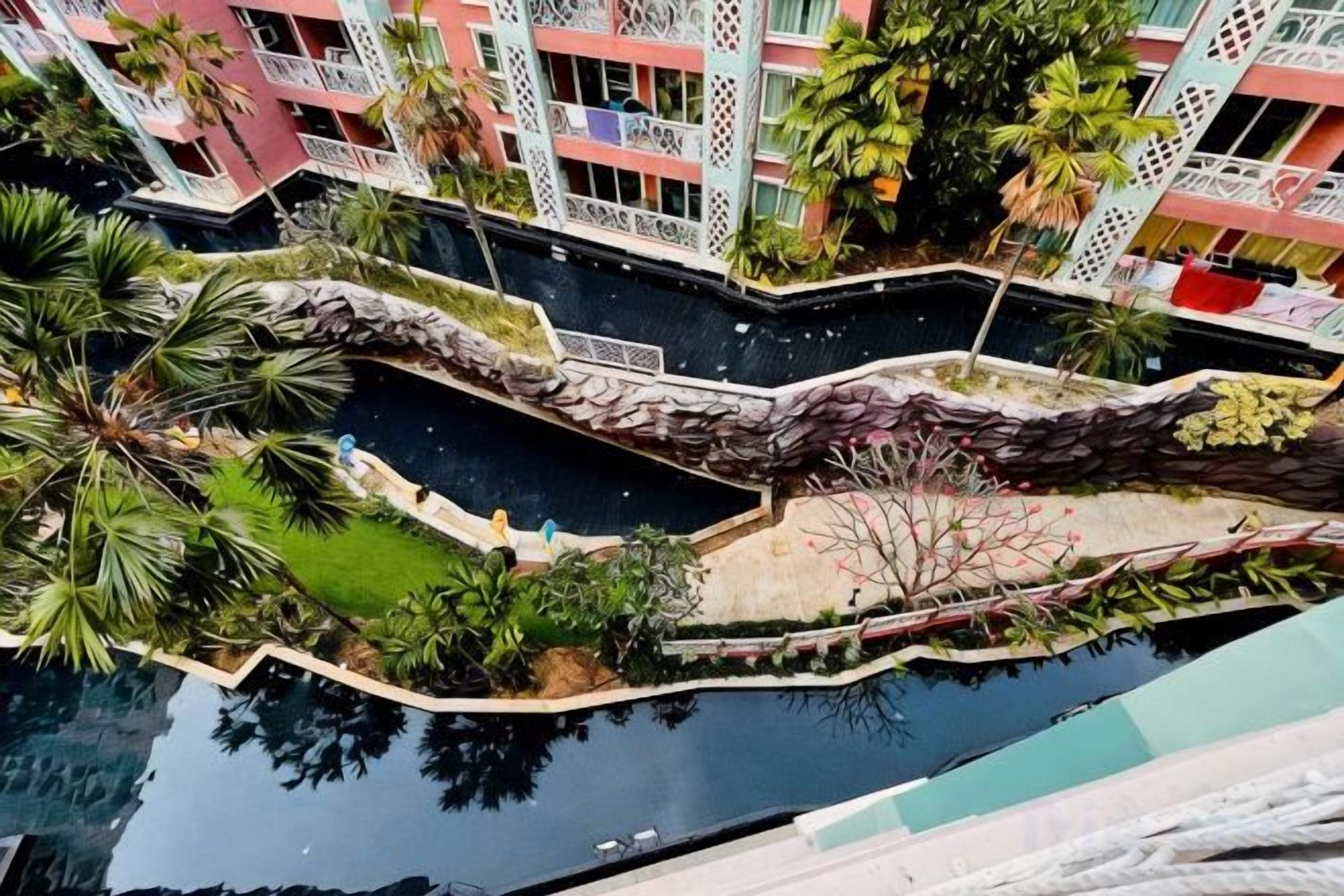 Un hotel de varios pisos con balcones, una fuente de agua y jardines tropicales.