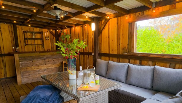 Une pièce chaleureuse avec un plafond en bois, une table en verre ornée d’un vase de fleurs, un canapé et un banc.