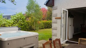 Un bain à remous avec des marches, une table en bois et deux chaises, le tout situé dans un jardin avec une maison et des arbres.