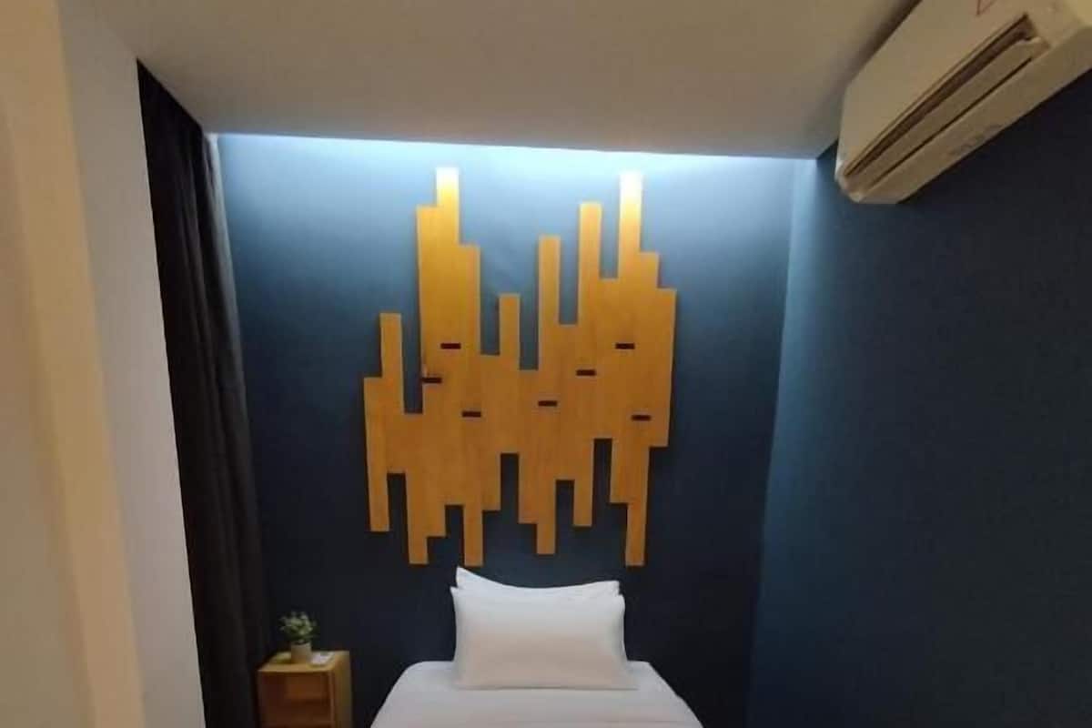 A hotel room with a bed, a wall-mounted air conditioner, and a small bedside table with a plant.