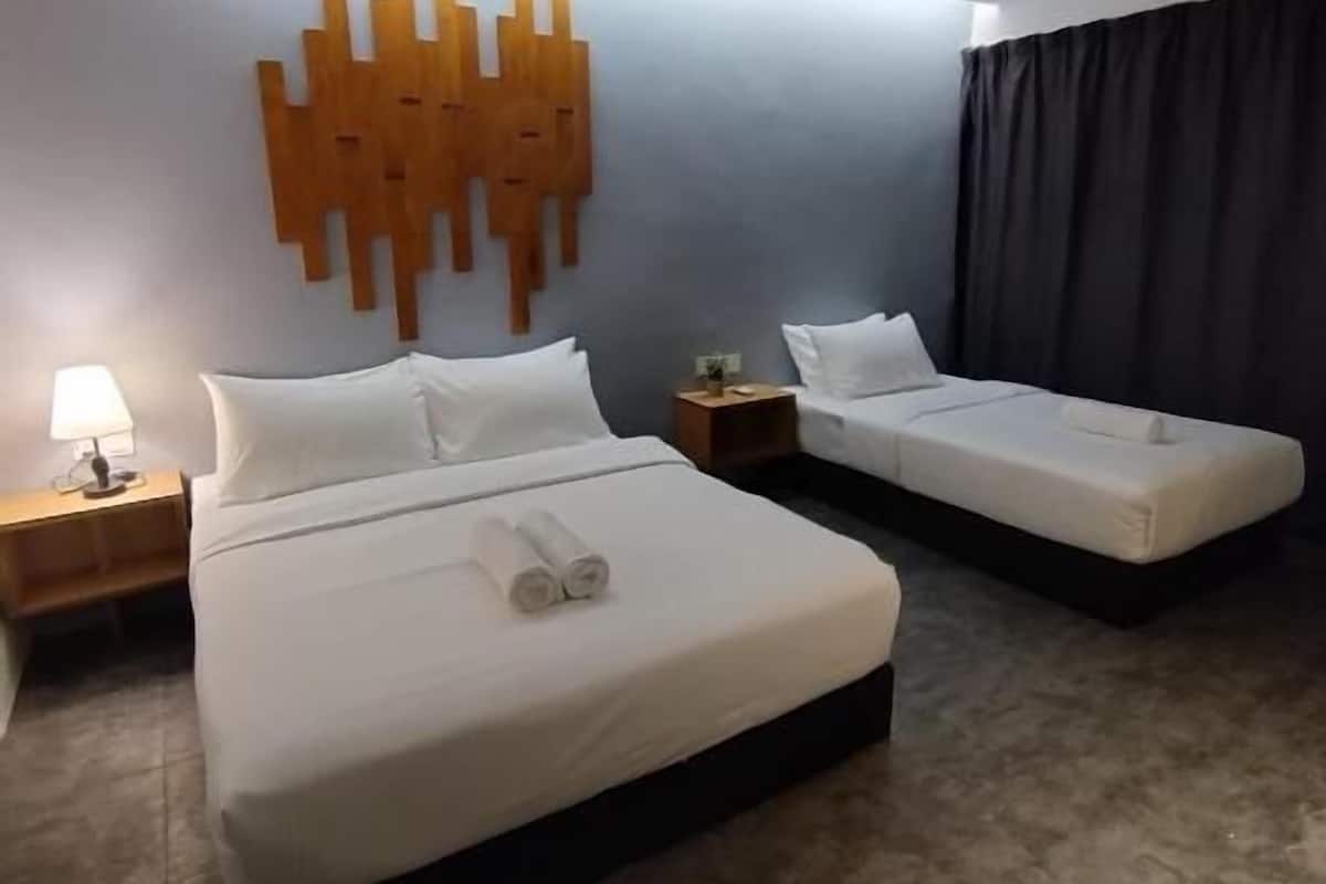 A hotel room with two beds, a wooden wall art piece, a nightstand with a lamp, and a dark curtain.