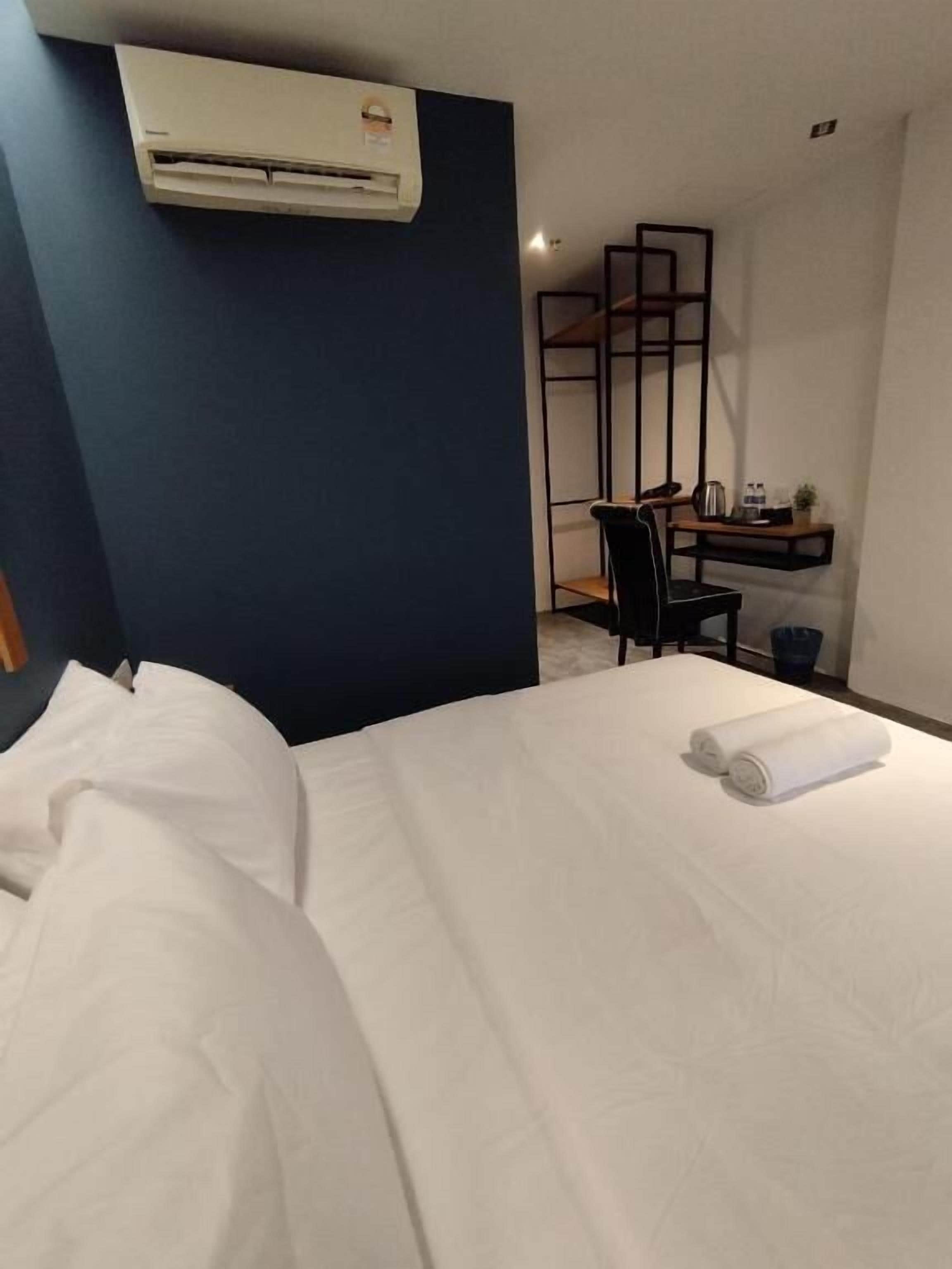 Een hotelkamer met een bed, een bureau, een stoel, een klein plankje en een airconditioning.