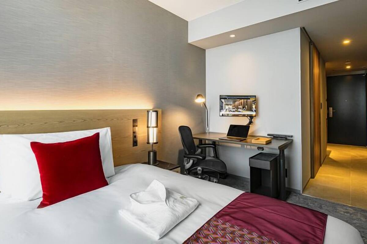 A hotel room with a bed, desk, chair, and a door leading to another room.