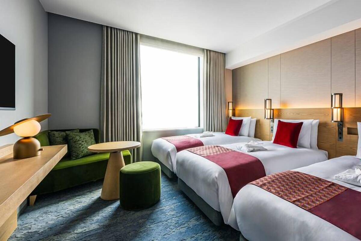 A hotel room with two beds, a green sofa, a small round table, and a large window with curtains.