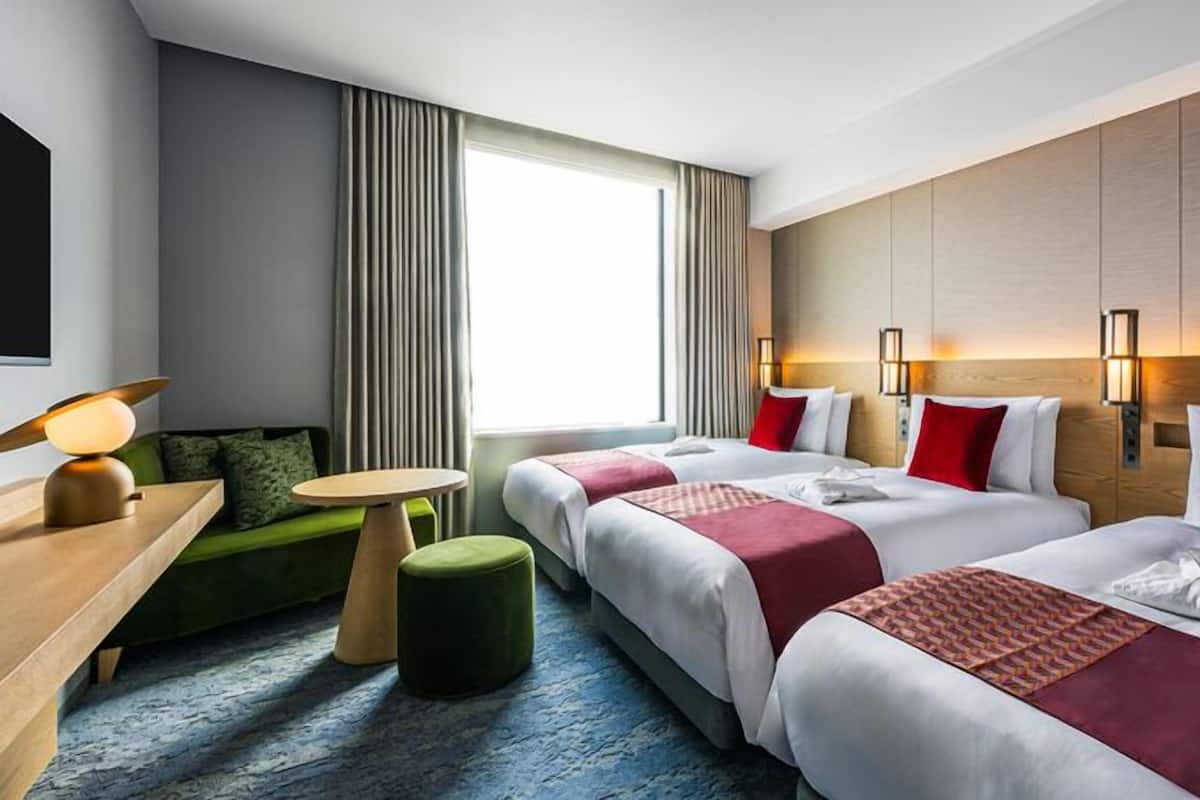 A hotel room with two beds, a green sofa, a small round table, and a large window with curtains.