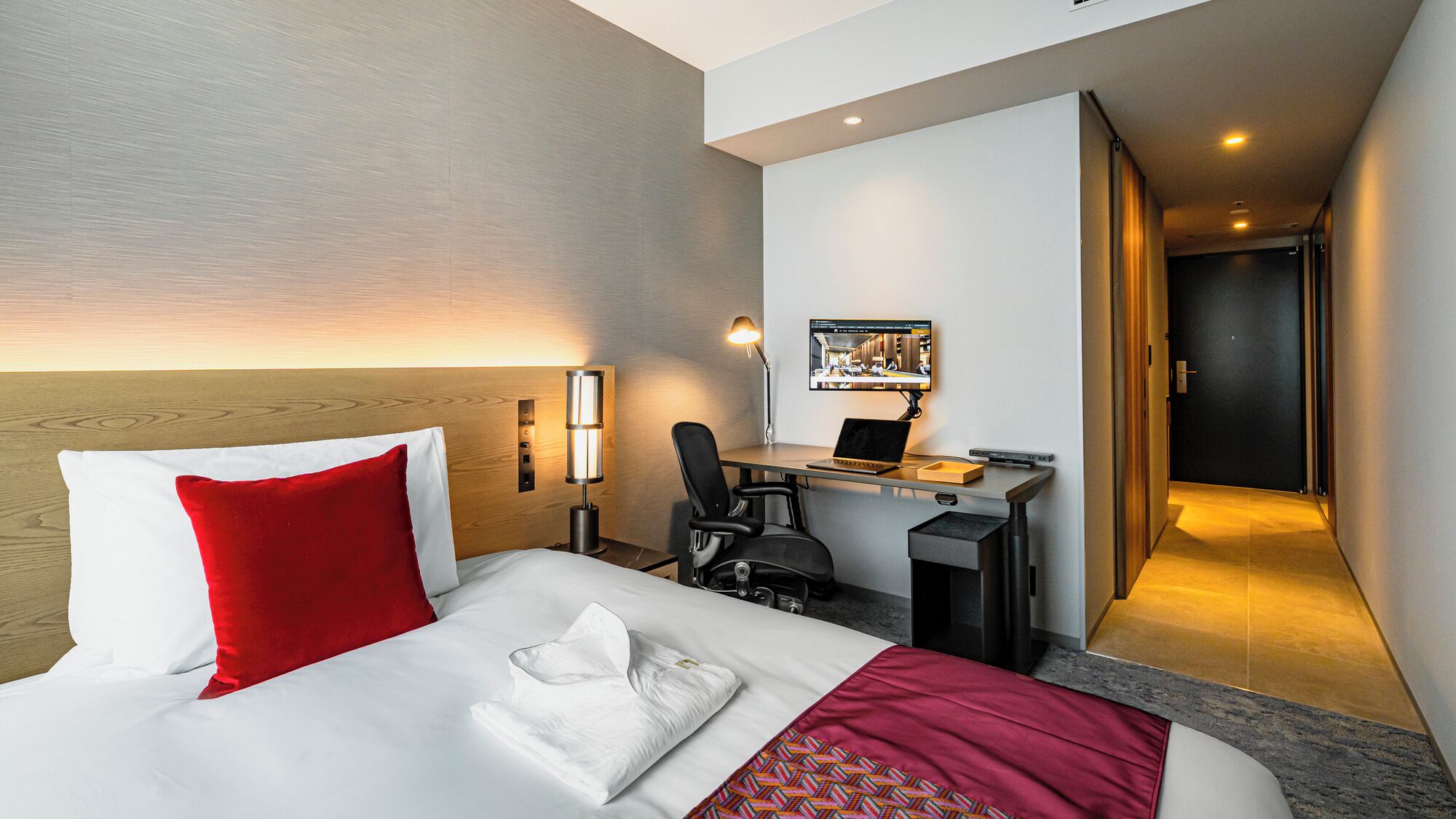 A hotel room with a bed, desk, chair, and a television.