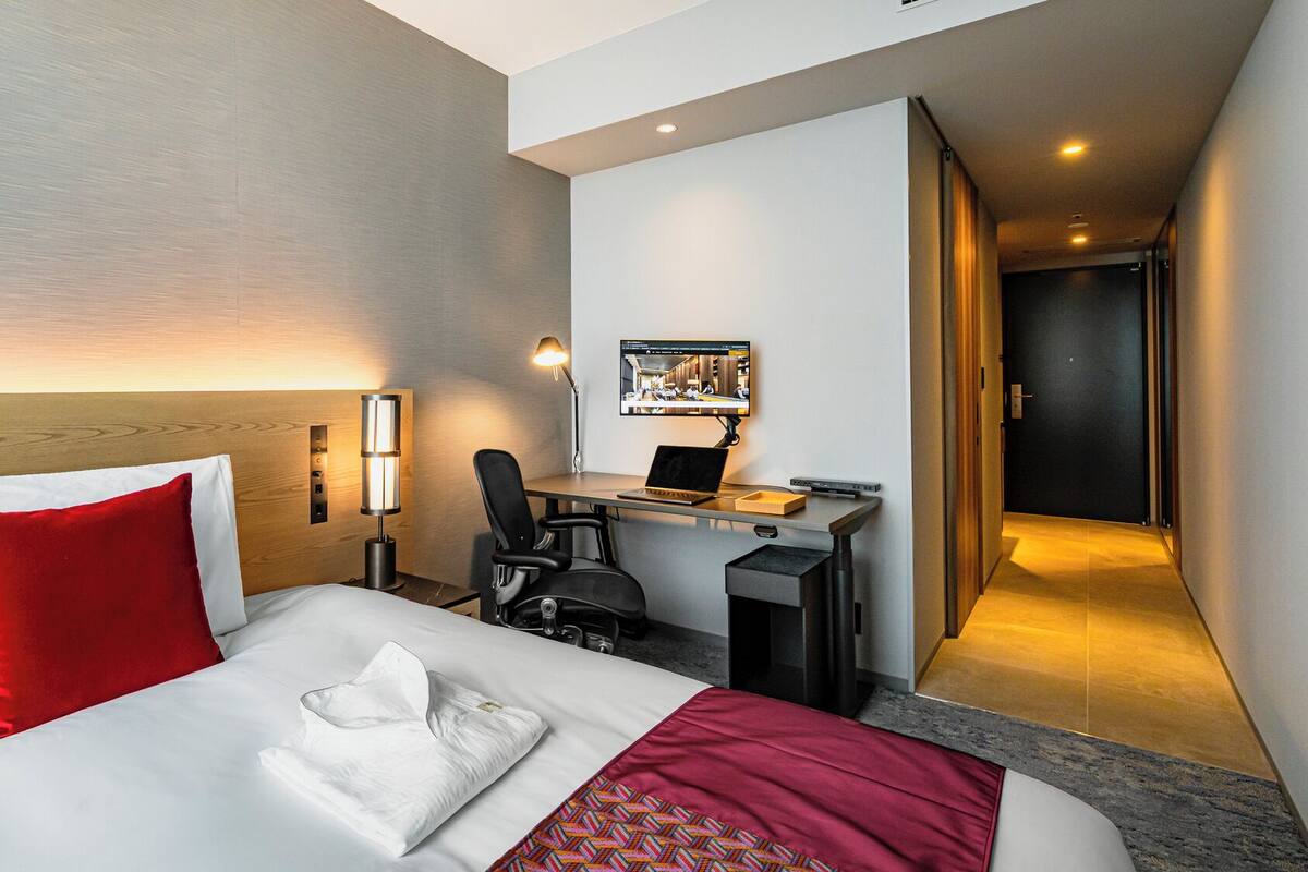 A hotel room with a bed, desk, chair, and a television.