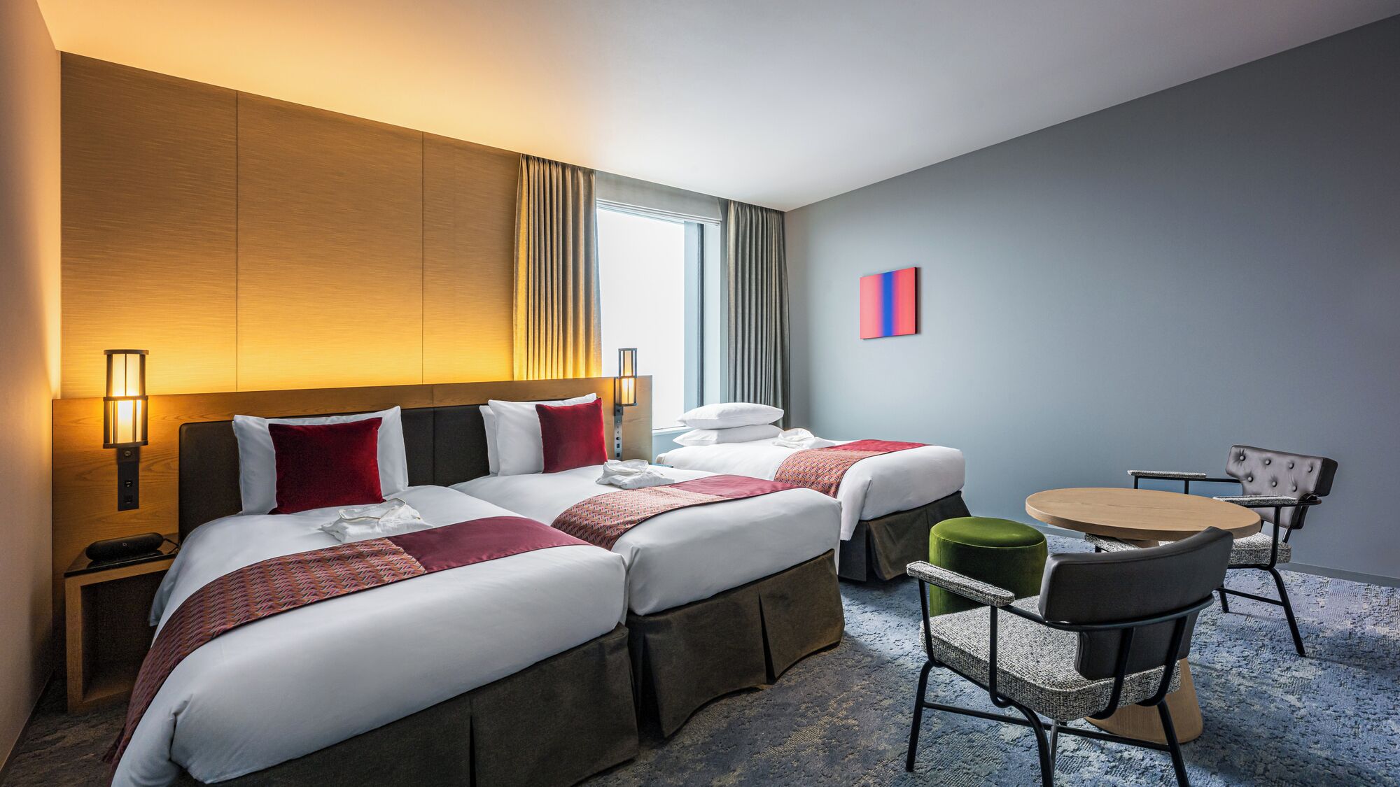 A hotel room with two beds, a desk, a chair, and a small table.