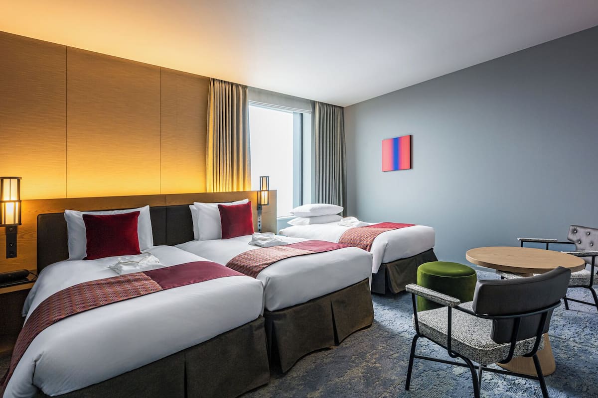 A hotel room with two beds, a desk, a chair, and a small table.