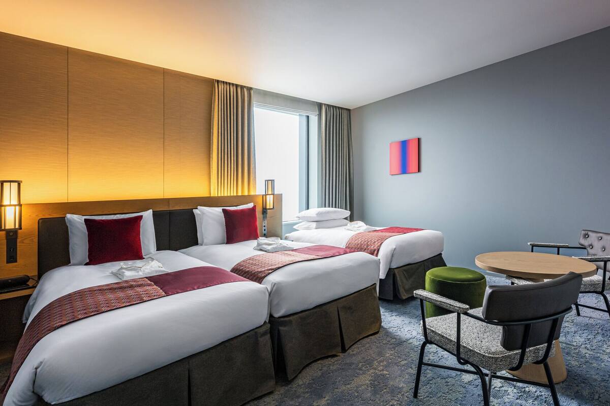 A hotel room with two beds, a desk, a chair, and a small table.